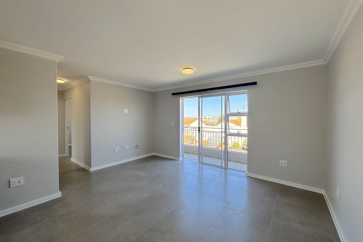 A bright, spacious, and empty living area featuring neutral tiled floors, modern finishes, and direct access to a private balcony through sliding glass doors.