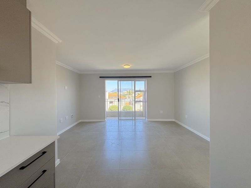 A bright, open-plan living area featuring neutral tiled flooring, modern cabinetry, and a sliding door leading to an outdoor balcony.