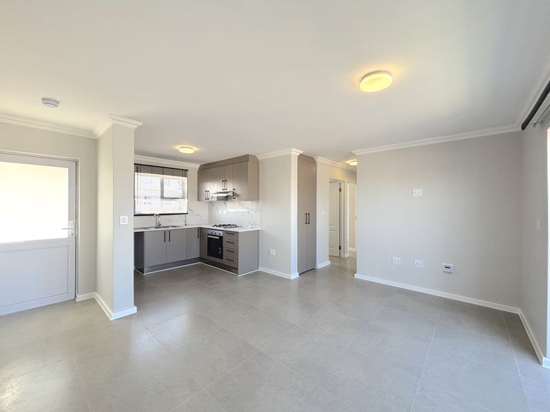 Modern open-plan living area featuring a sleek kitchen with built-in appliances, neutral tiled flooring, and clean finishes throughout this bright, vacant apartment space.