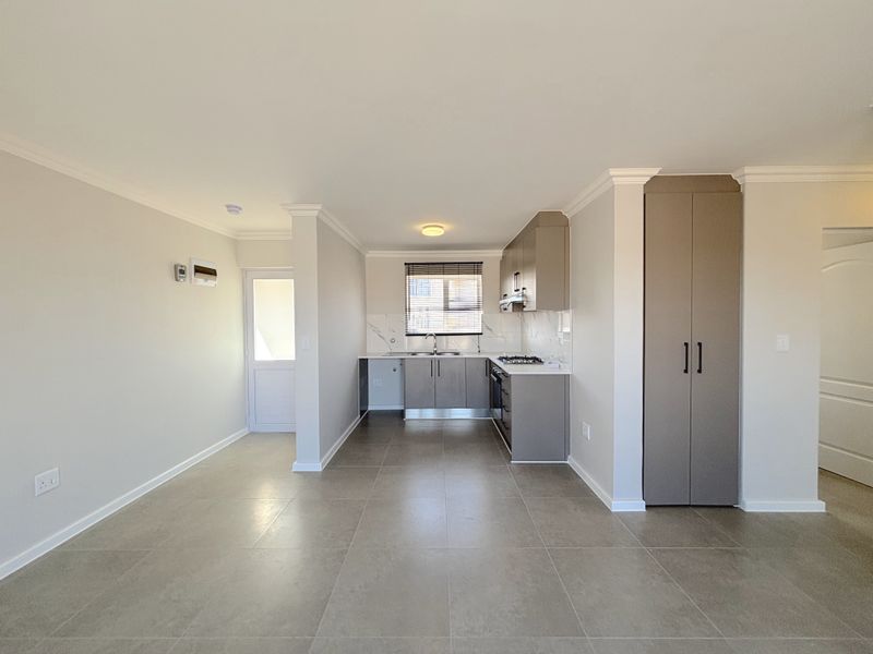 Modern open-plan kitchen and living area featuring neutral tones, tiled flooring, built-in cabinetry, and a gas hob, offering a clean and functional space.