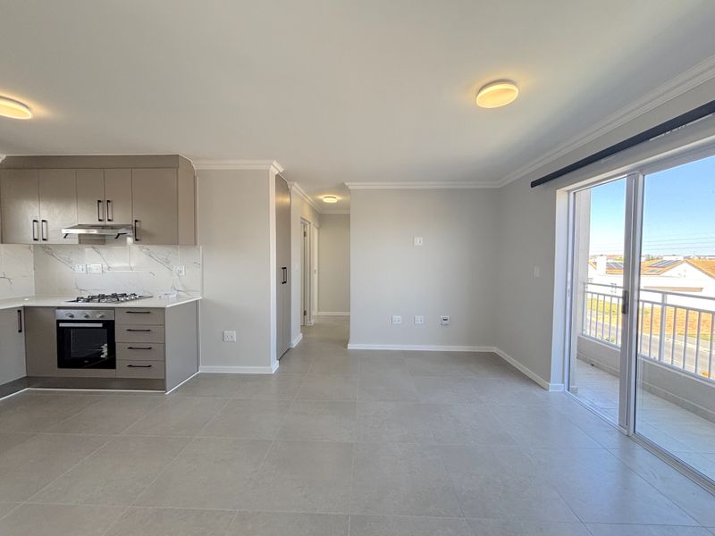 Modern open-plan kitchen and living area featuring sleek cabinetry, integrated appliances, tiled flooring, and direct access to a private balcony.