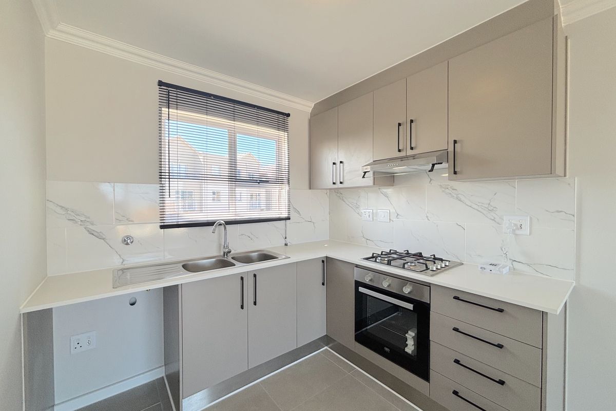 Modern kitchen featuring sleek grey cabinetry, marble-look splashbacks, a gas hob, built-in oven, and stainless steel sink with ample counter space.