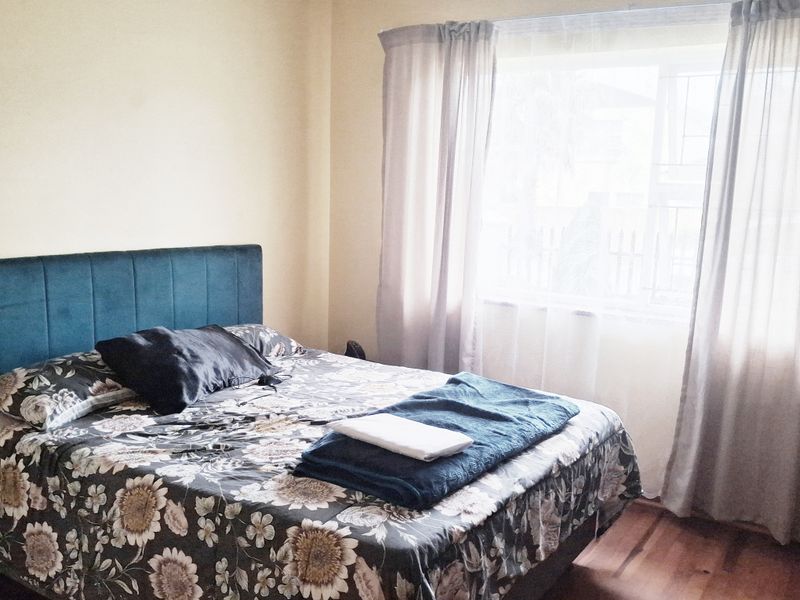 A bedroom featuring laminate flooring and a large window with installed curtain rails, providing natural light to the space.