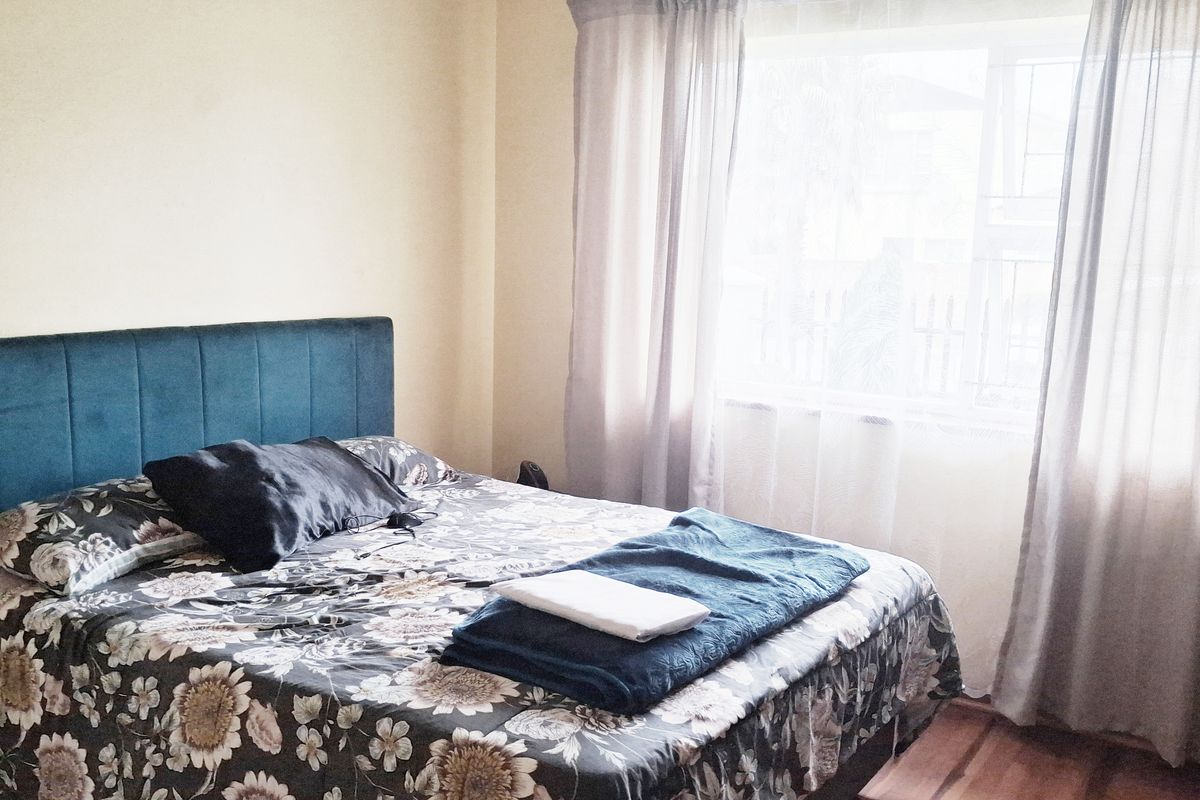 A bedroom featuring laminate flooring and a large window with installed curtain rails, providing natural light to the space.