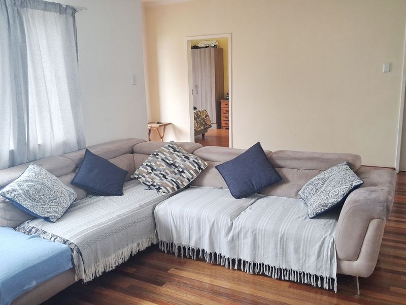 A living room featuring hardwood flooring and a view into an adjacent bedroom.
