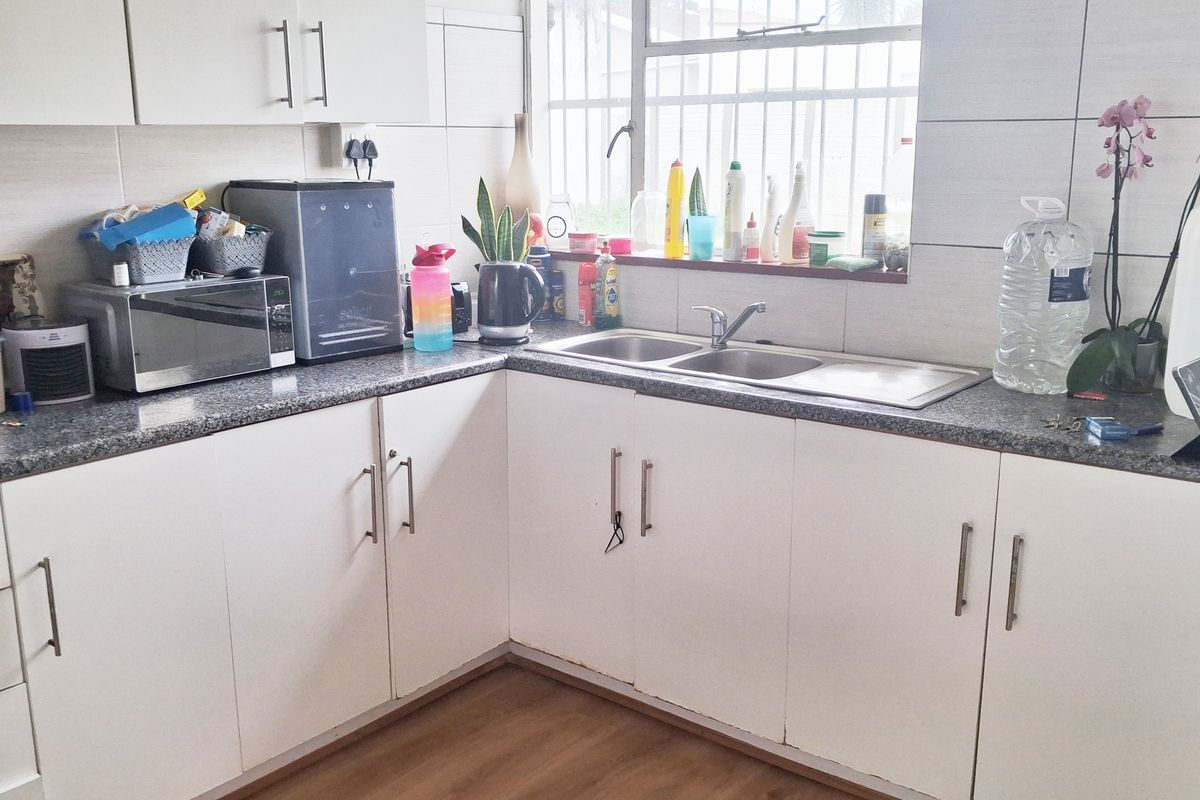 A functional kitchen featuring white cabinetry, granite countertops, a double bowl stainless steel sink, and a tiled backsplash with window security bars.