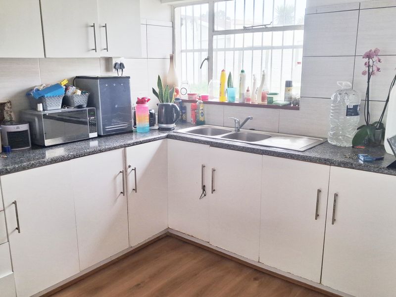 A functional kitchen featuring white cabinetry, granite countertops, a double bowl stainless steel sink, and a tiled backsplash with window security bars.
