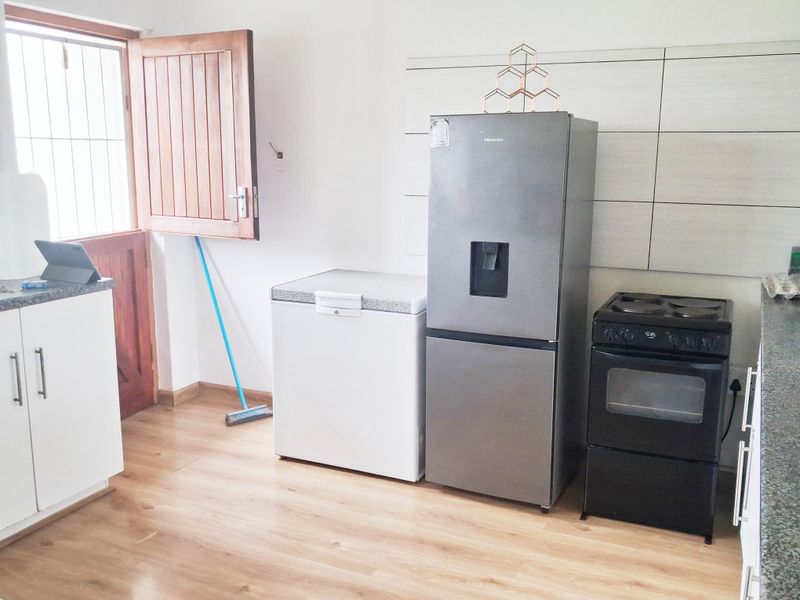 A functional kitchen area featuring laminate flooring, tiled splashbacks, and built-in cabinetry with direct access to the exterior via a solid wood door.