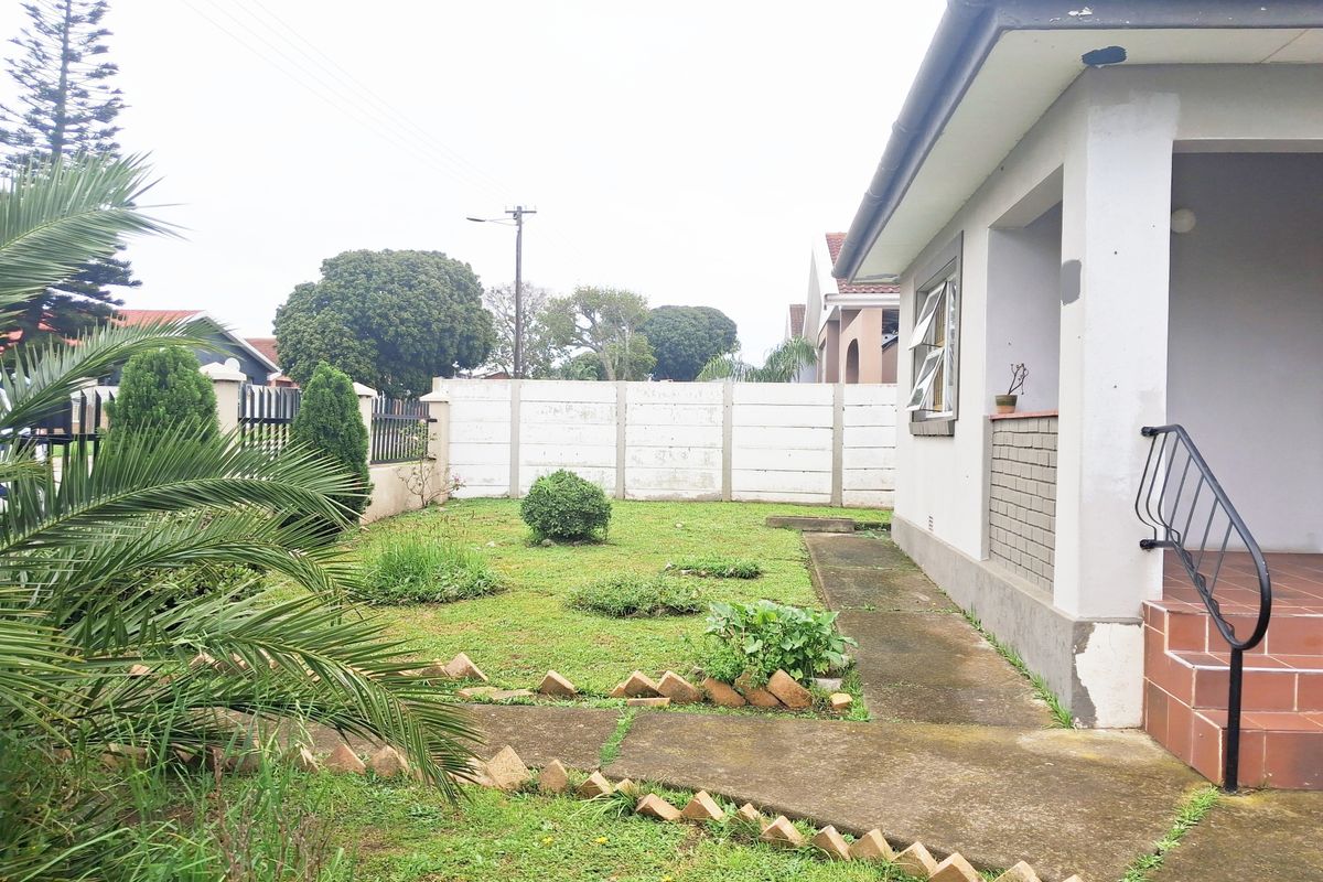 Rear garden area featuring a concrete pathway, tiled porch with metal handrail, and perimeter boundary walling.
