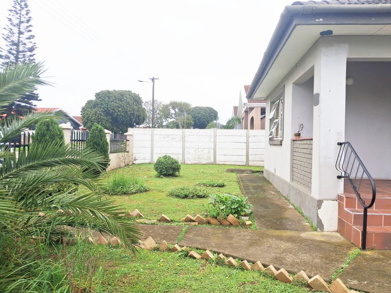 Rear garden area featuring a concrete pathway, tiled porch with metal handrail, and perimeter boundary walling.
