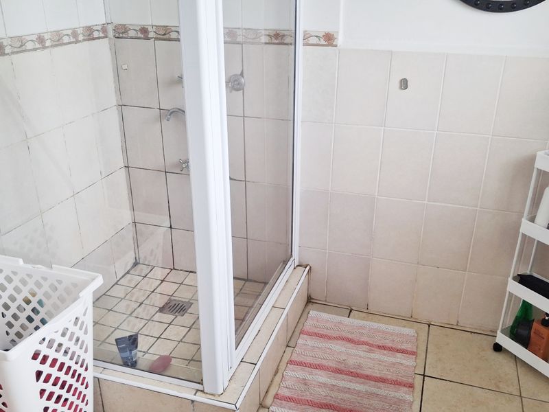A functional bathroom featuring a glass-enclosed shower with tiled walls and flooring, showing signs of wear and dated finishes.