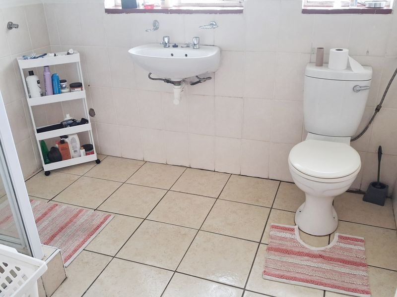 A functional bathroom featuring a wall-mounted basin, close-coupled toilet, and shower enclosure with tiled walls and flooring.