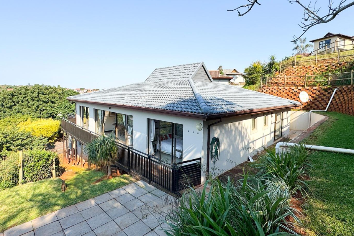 Rear view of the house featuring a tiled roof, paved patio area, and a terraced garden with a retaining wall.
