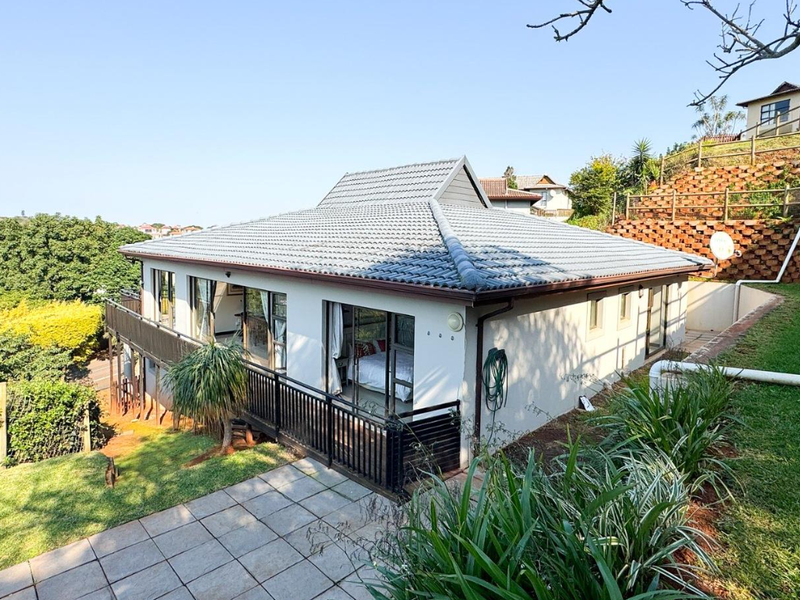 Rear view of the house featuring a tiled roof, paved patio area, and a terraced garden with a retaining wall.