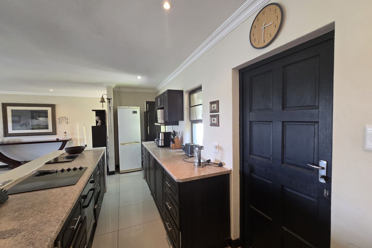 Modern kitchen featuring dark cabinetry, granite countertops, integrated hob, and tiled flooring, seamlessly flowing into the adjacent living area.