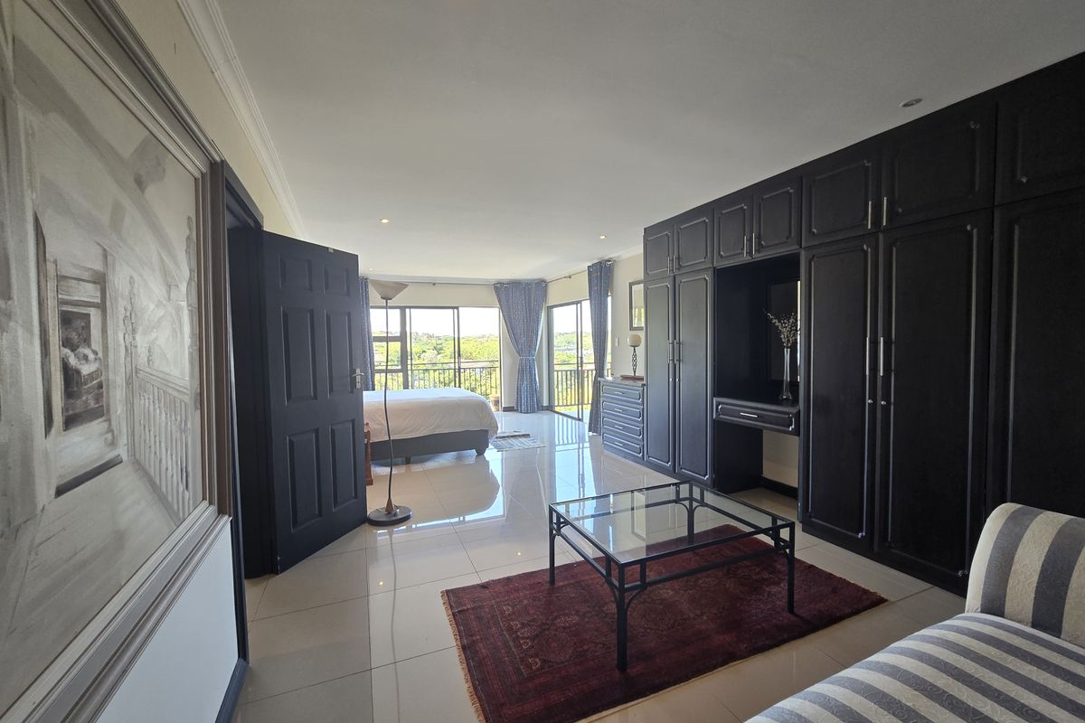 Spacious bedroom featuring large built-in cupboards, polished tiled flooring, and sliding glass doors leading to a private balcony with scenic views.
