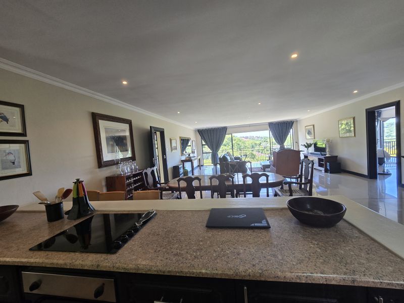 Spacious open-plan living and dining area featuring a kitchen with granite countertops, electric hob, and seamless flow to a balcony with scenic views.