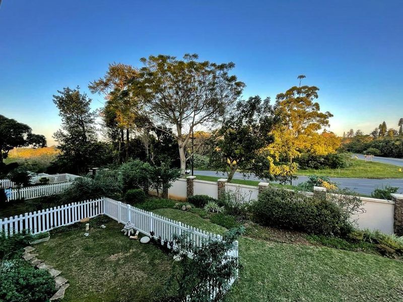 A view of a well-maintained rear garden featuring a white picket fence and a solid masonry boundary wall with mature trees.