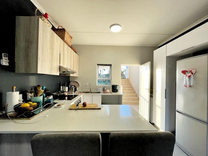 Modern kitchen featuring light wood-grain cabinetry, sleek stone countertops, integrated appliances, and a functional layout with direct access to an outdoor staircase.