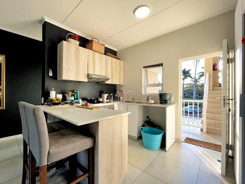 Modern kitchen featuring light wood-finish cabinetry, a breakfast bar, and tiled flooring, with direct access to an outdoor balcony area.