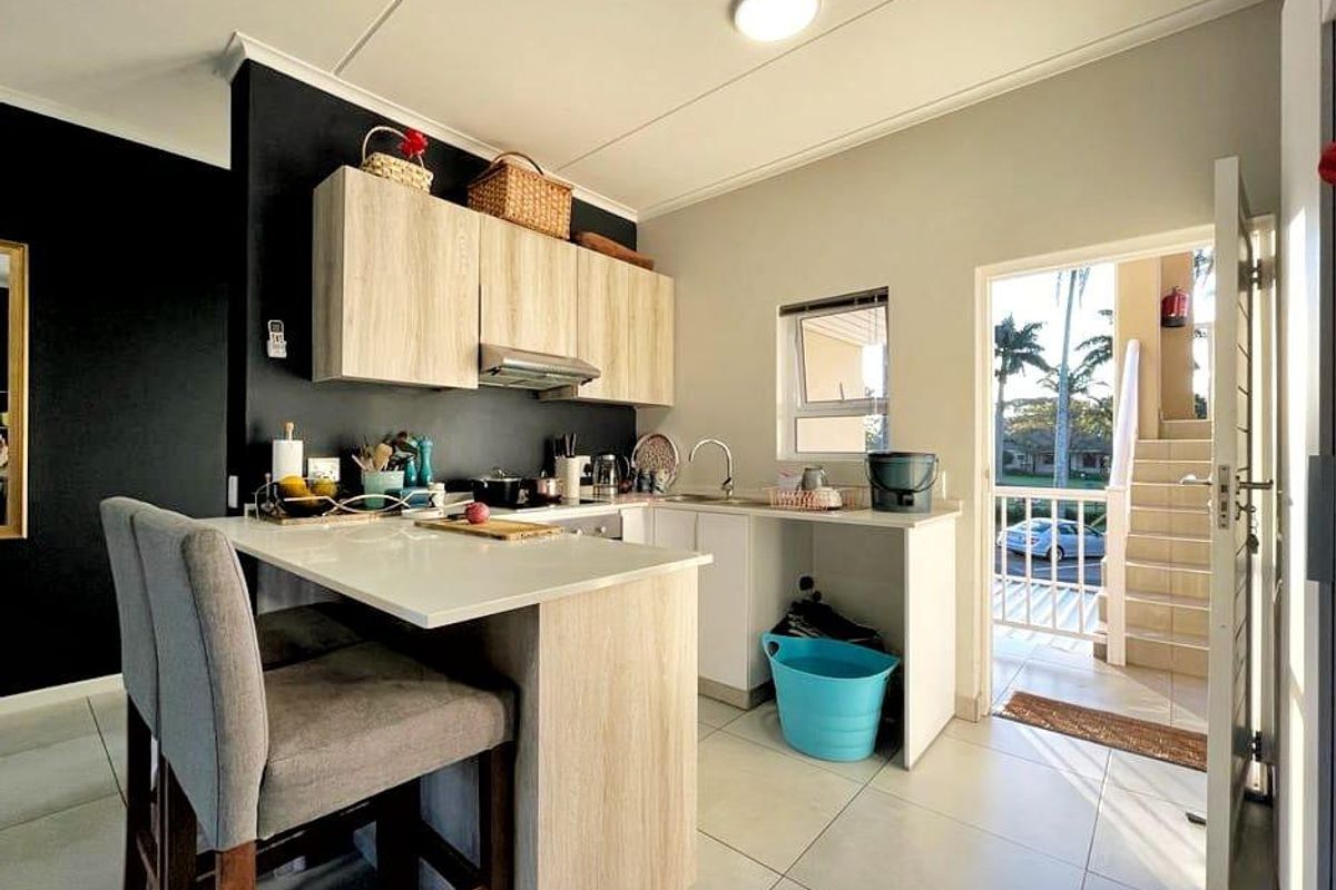 Modern kitchen featuring light wood-finish cabinetry, a breakfast bar, and tiled flooring, with direct access to an outdoor balcony area.