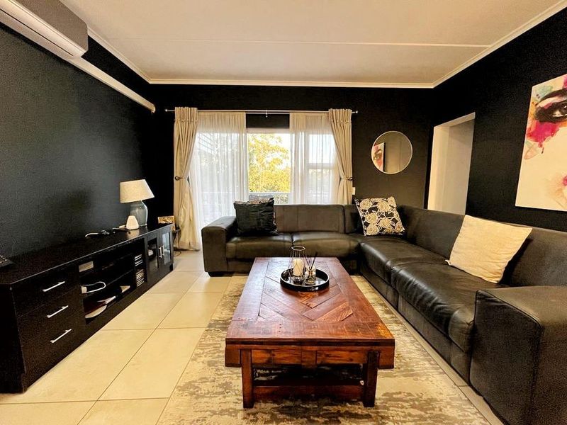 A well-maintained living room featuring dark accent walls, large format floor tiles, and a sliding glass door providing access to the balcony.