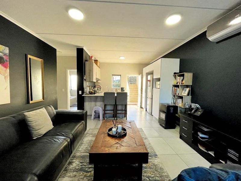 Open-plan living and kitchen area featuring tiled flooring, modern dark accent walls, and a functional kitchen layout with an island breakfast bar.