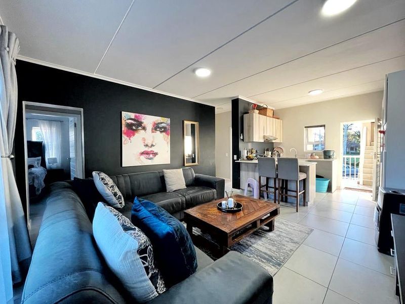 Open-plan living area featuring a modern kitchen with island, tiled flooring, and neutral finishes, seamlessly connecting to the lounge space.