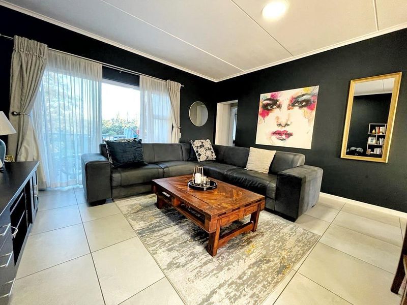 A well-maintained living room featuring large format floor tiles, dark accent walls, and a sliding glass door providing access to an outdoor area.