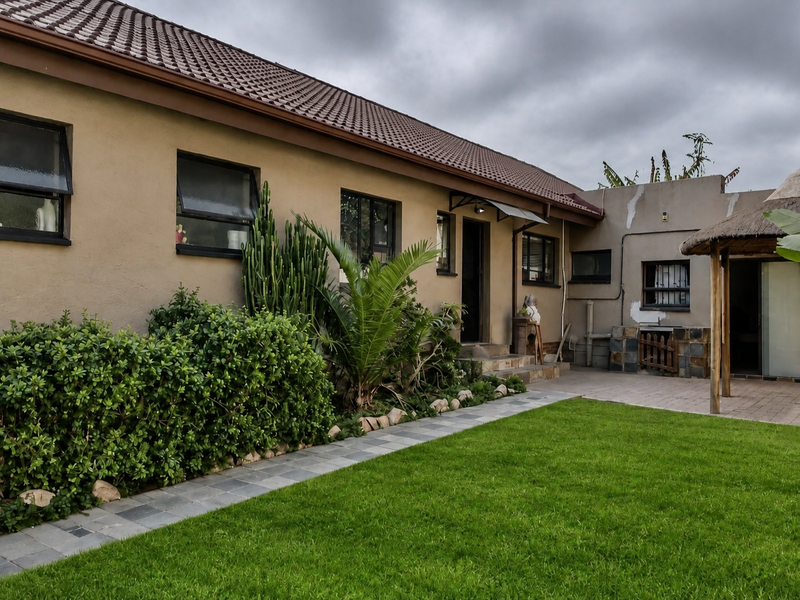 Rear view of the property featuring a paved patio, a thatched lapa, and a well-maintained garden area with established landscaping.