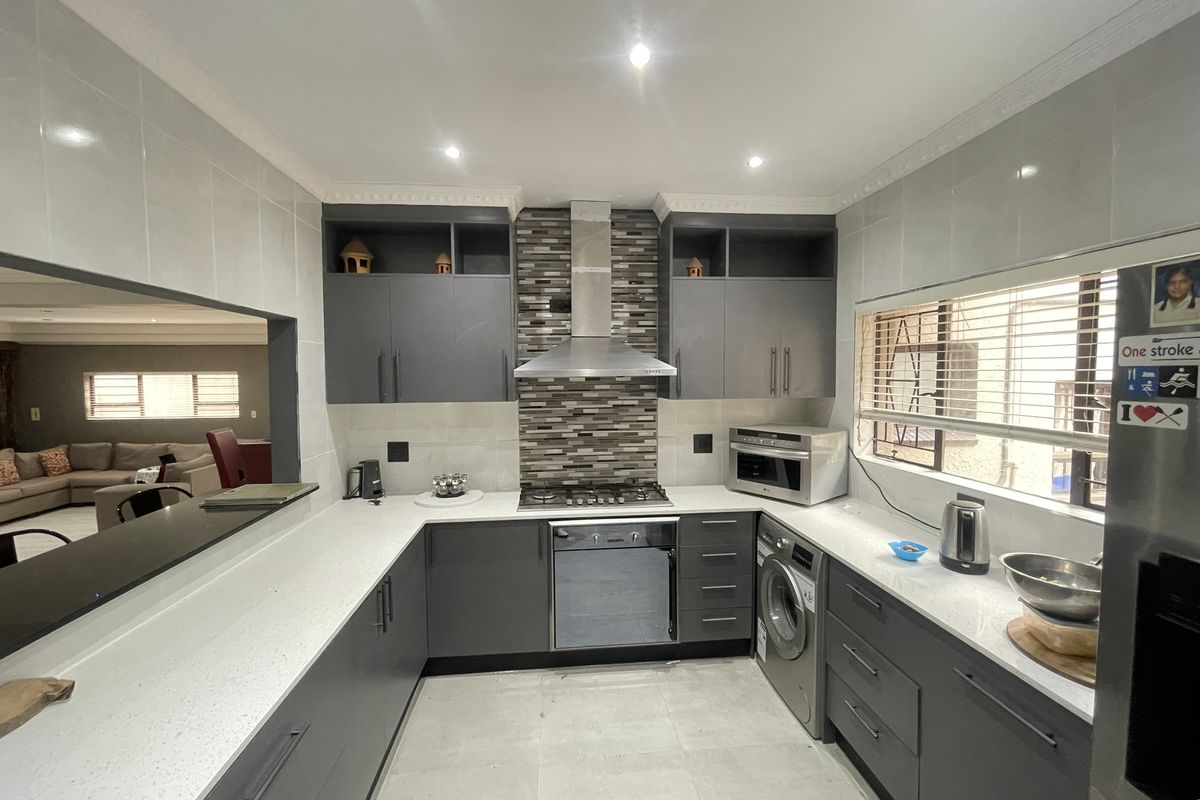 Modern kitchen featuring dark grey cabinetry, white quartz countertops, a gas hob with extractor, and integrated laundry appliances with a convenient serving hatch.