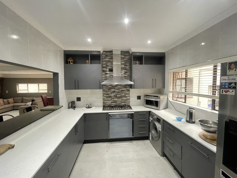 Modern kitchen featuring dark grey cabinetry, white quartz countertops, a gas hob with extractor, and integrated laundry appliances with a convenient serving hatch.