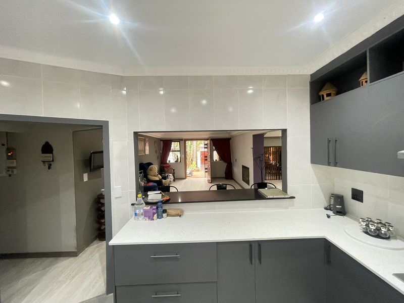 Modern kitchen featuring sleek grey cabinetry, white quartz countertops, and a convenient pass-through window overlooking the living area.