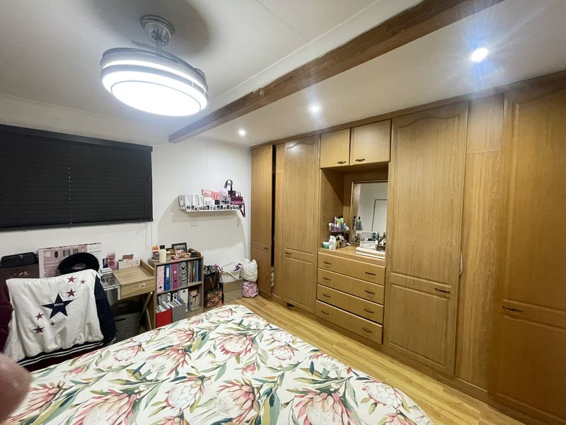 A bedroom featuring extensive built-in wooden cabinetry with integrated vanity, laminate flooring, and a ceiling fan.