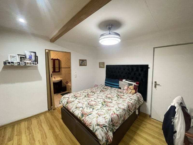 A bedroom featuring laminate flooring, an exposed ceiling beam, and an en-suite bathroom, providing a functional and comfortable living space.