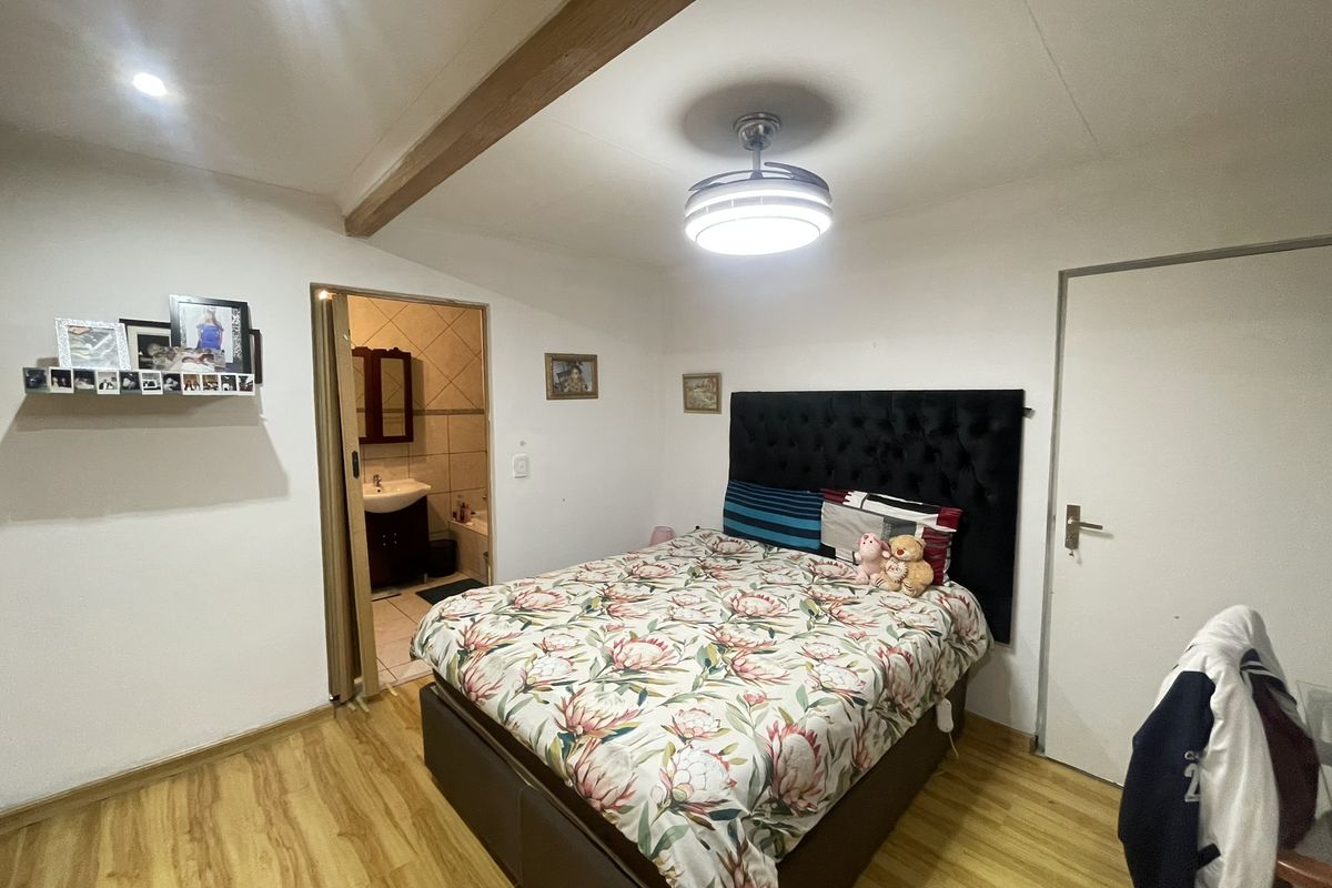 A bedroom featuring laminate flooring, an exposed ceiling beam, and an en-suite bathroom, providing a functional and comfortable living space.