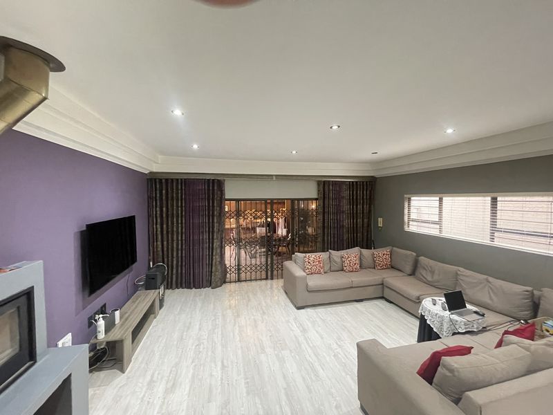 Spacious living room featuring a fireplace, recessed downlighting, modern laminate flooring, and large sliding doors with security gates leading to the patio.