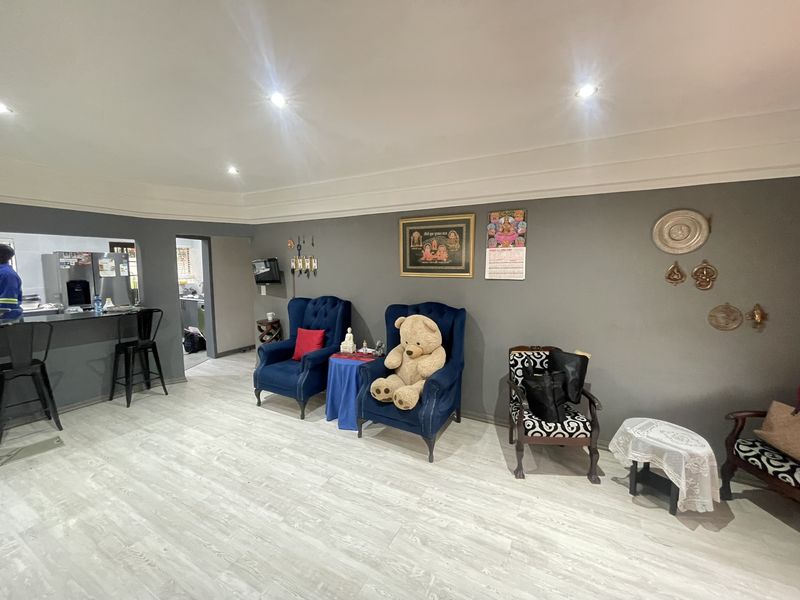 Open plan living area featuring modern laminate flooring, recessed downlighting, coved ceilings, and a breakfast bar overlooking the kitchen area.