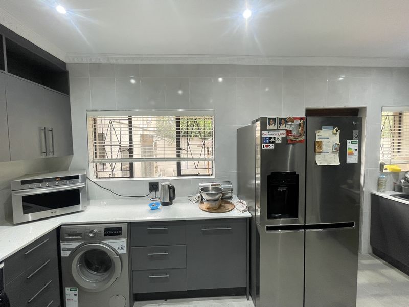 Modern kitchen featuring sleek grey cabinetry, stone countertops, tiled backsplash, and integrated appliances including a built-in microwave and washing machine.