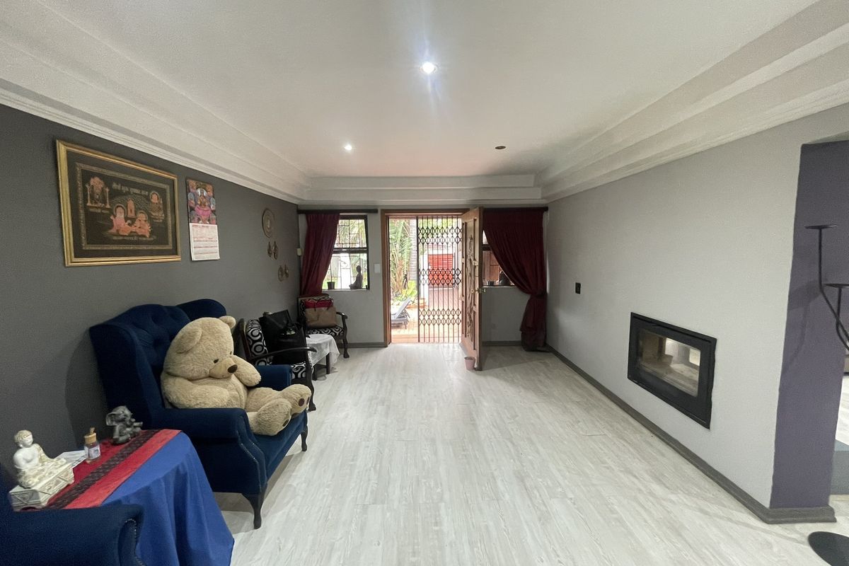 A spacious living room featuring light laminate flooring, a built-in fireplace, and direct access to an outdoor area through a security gate.