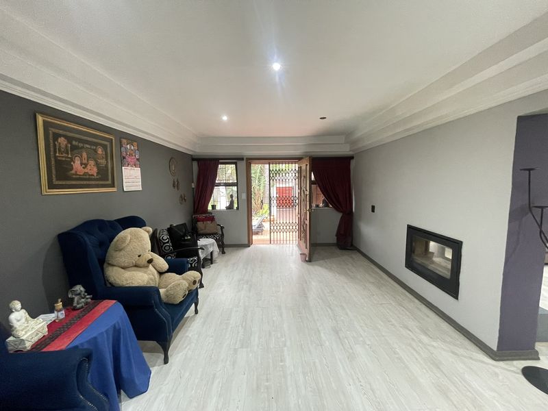 A spacious living room featuring light laminate flooring, a built-in fireplace, and direct access to an outdoor area through a security gate.