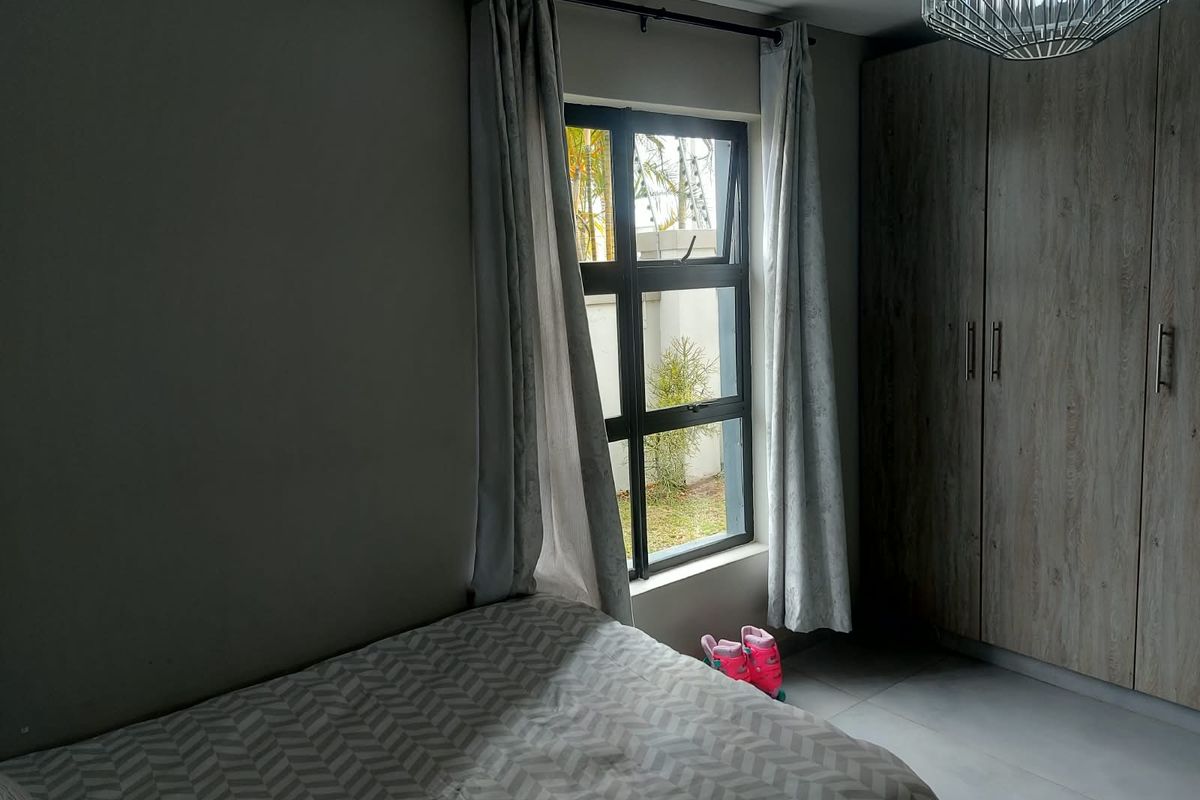 A well-maintained bedroom featuring built-in wooden cupboards, tiled flooring, and a window providing natural light.
