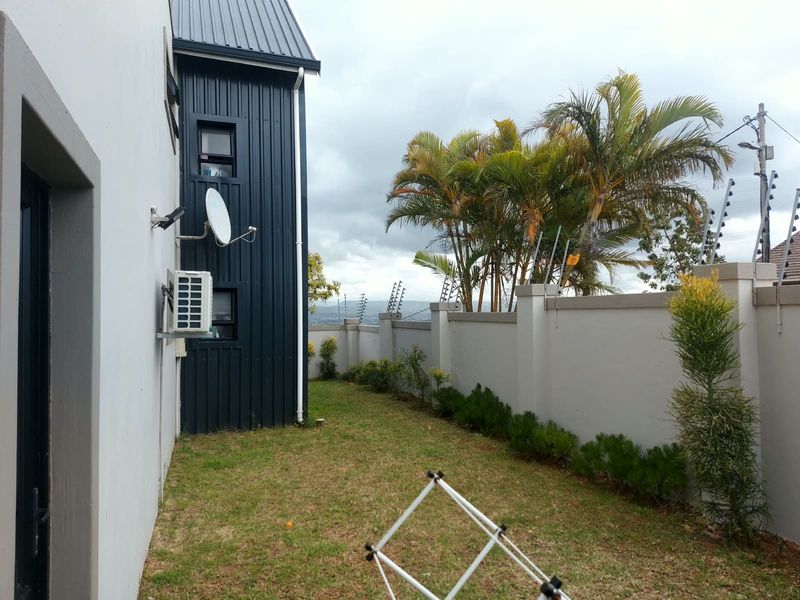 A view of the rear exterior area featuring a lawn, boundary wall with electric fencing, and modern metal cladding on the building facade.