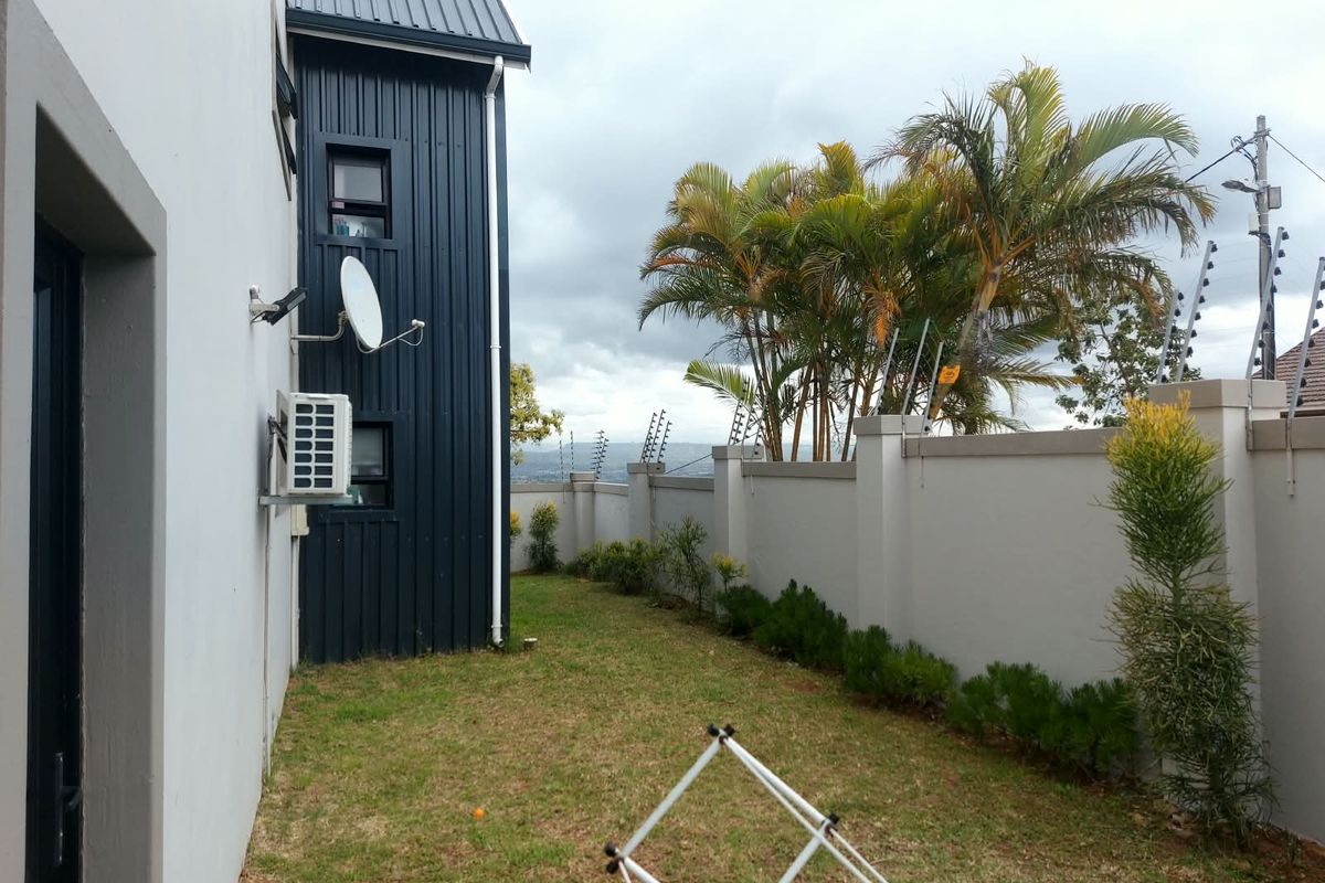 A view of the rear exterior area featuring a lawn, boundary wall with electric fencing, and modern metal cladding on the building facade.