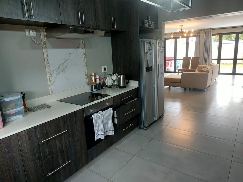 Modern open-plan kitchen featuring dark wood cabinetry, stone countertops, and integrated appliances, flowing seamlessly into a spacious living area with large floor tiles.