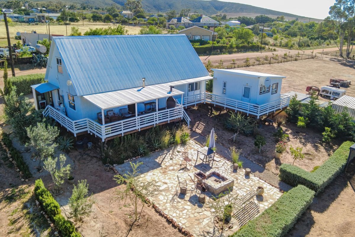 Aerial view of a rural property featuring a main house with a corrugated metal roof, raised timber decking, and a stone-paved outdoor entertainment area.