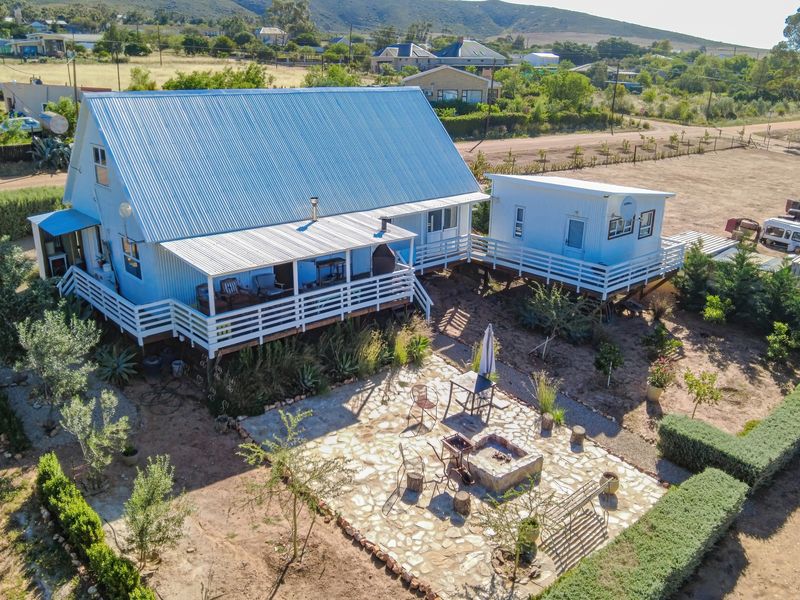 Aerial view of a rural property featuring a main house with a corrugated metal roof, raised timber decking, and a stone-paved outdoor entertainment area.