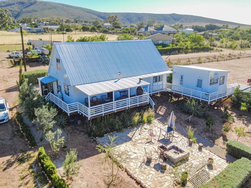 Aerial view of a detached house featuring a corrugated metal roof, a raised timber deck, and a stone-paved outdoor patio area with a fire pit.