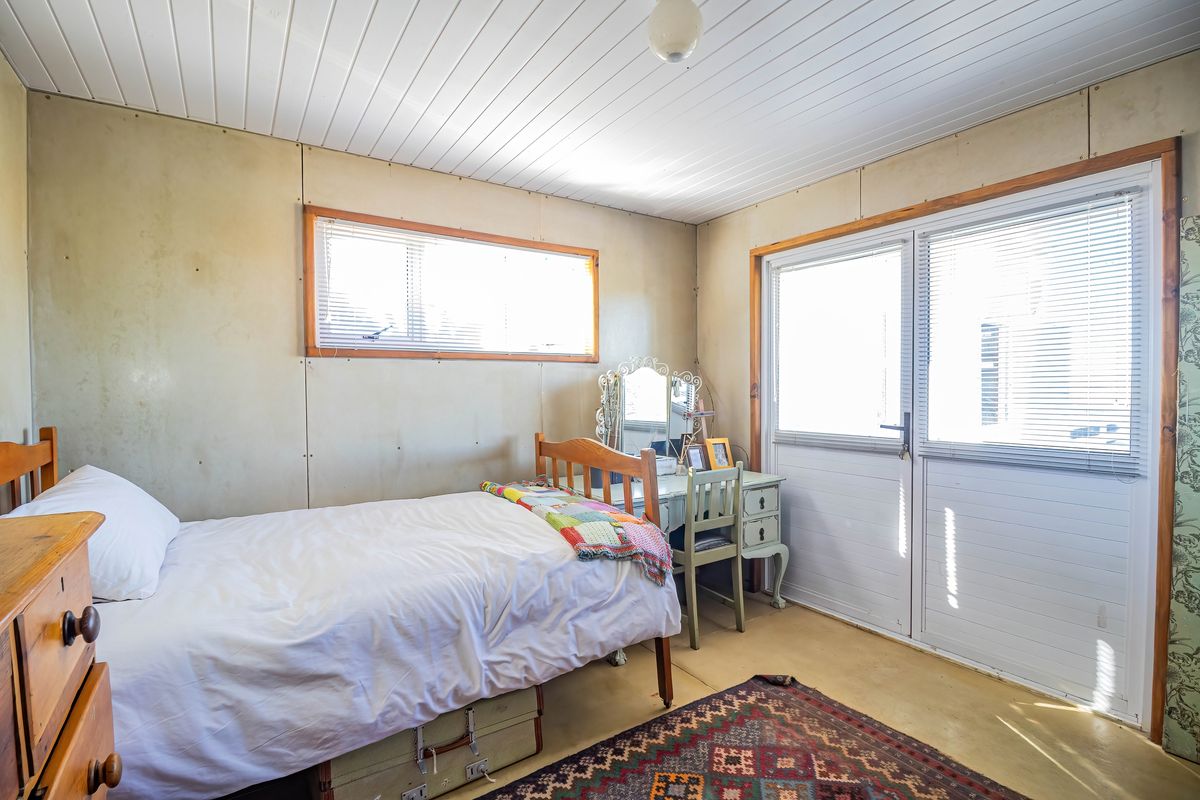 A bedroom featuring panelled walls, a tongue and groove ceiling, and direct access to the outdoors via a sliding glass door.