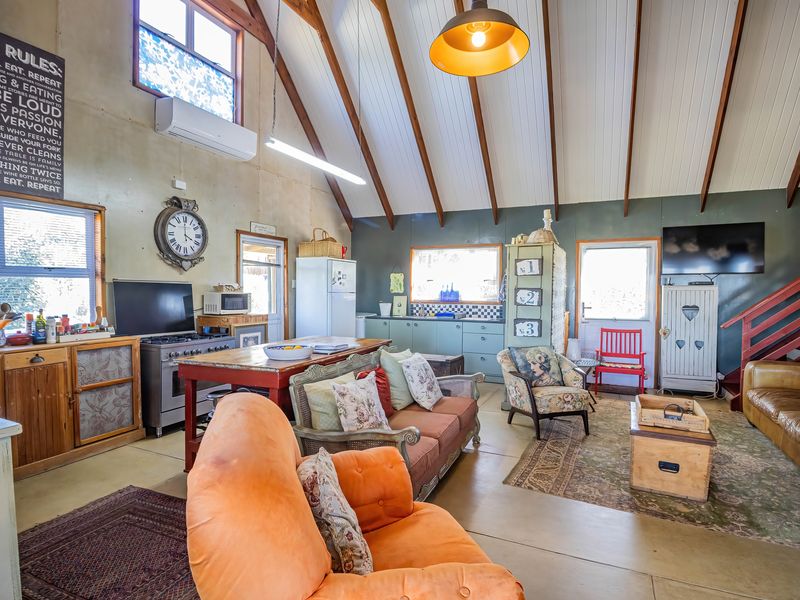 Spacious open-plan living area featuring a vaulted ceiling with exposed timber beams, integrated kitchen, and direct access to the upper level via a staircase.